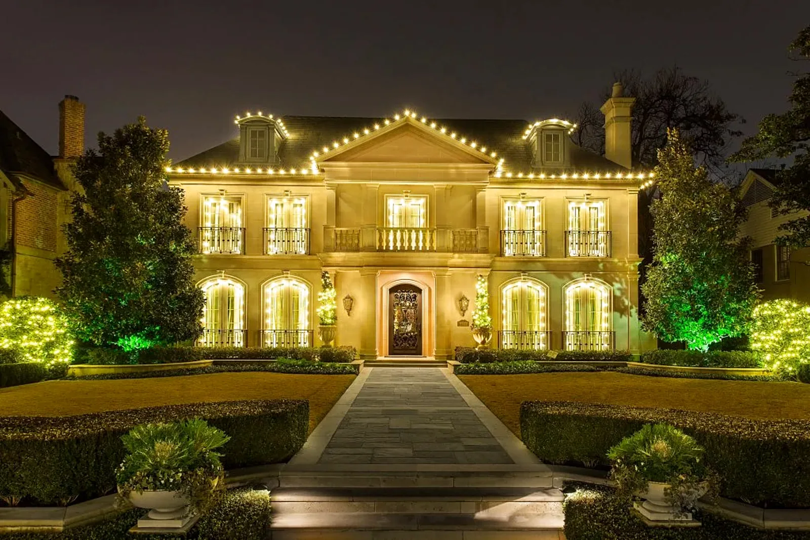 Two-story home with warm white roofline lighting and lit landscaping